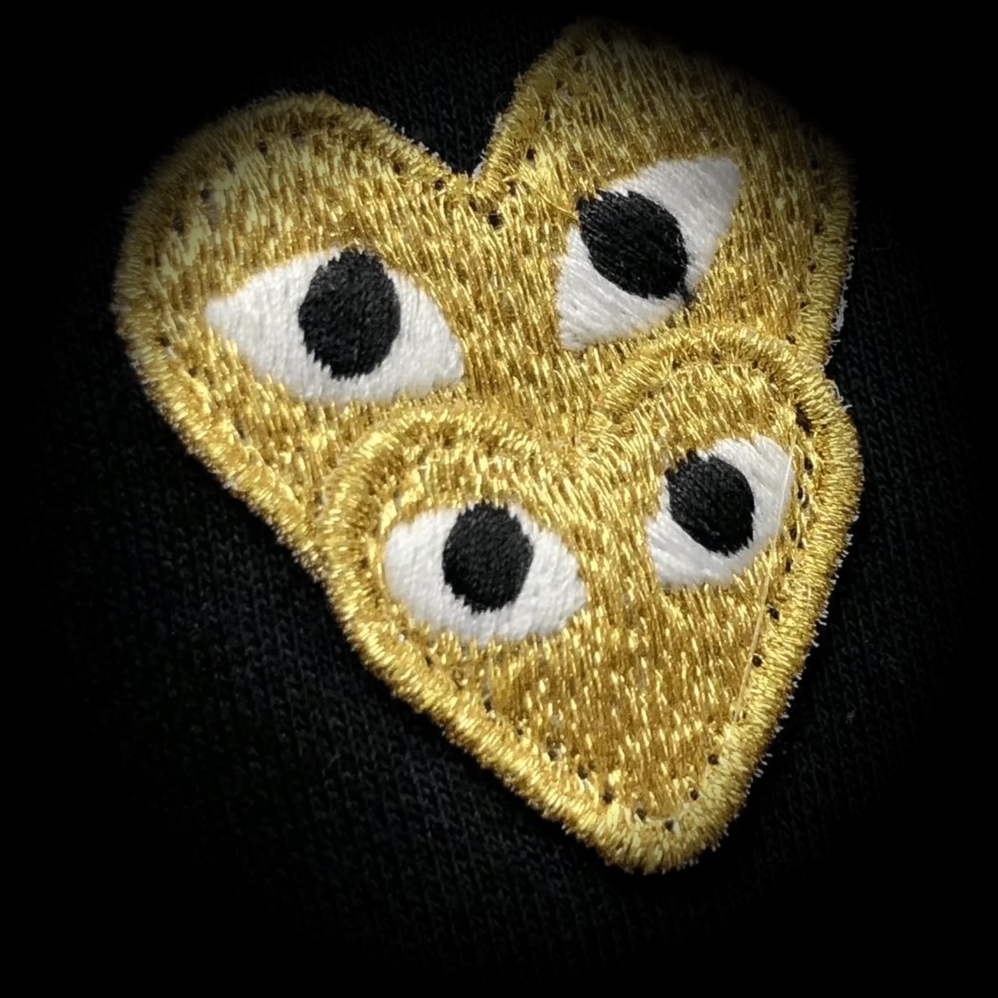 Patch bordado de dois corações dourados com olhos sobre tecido preto